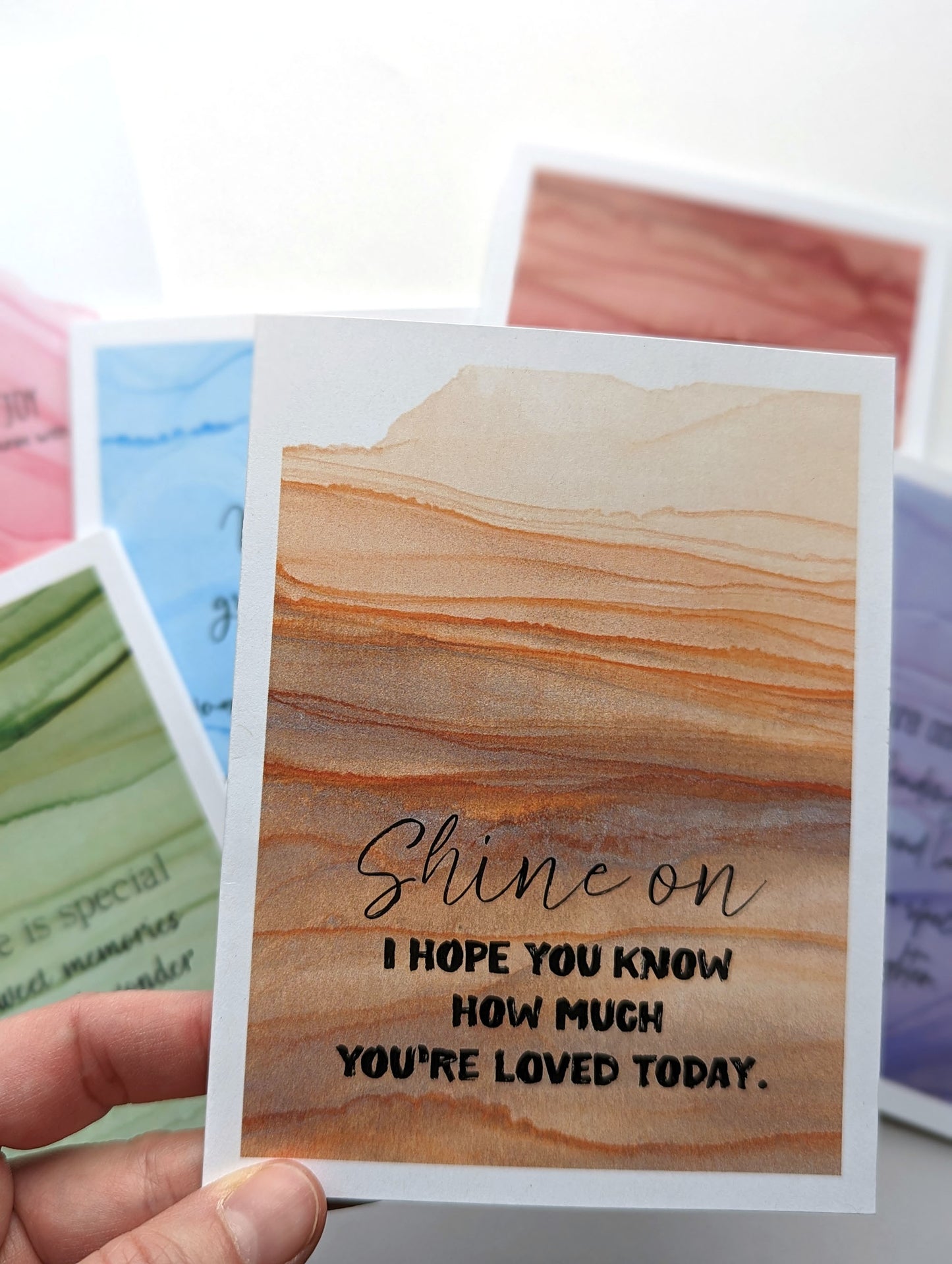 Hand holding the greeting card above the stack of others in the collection.