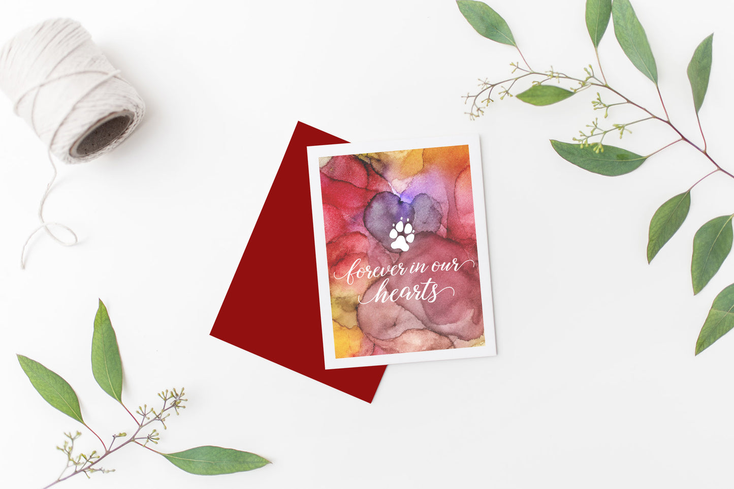 Greeting card laying on a white background near green leaves and a spool of white string.