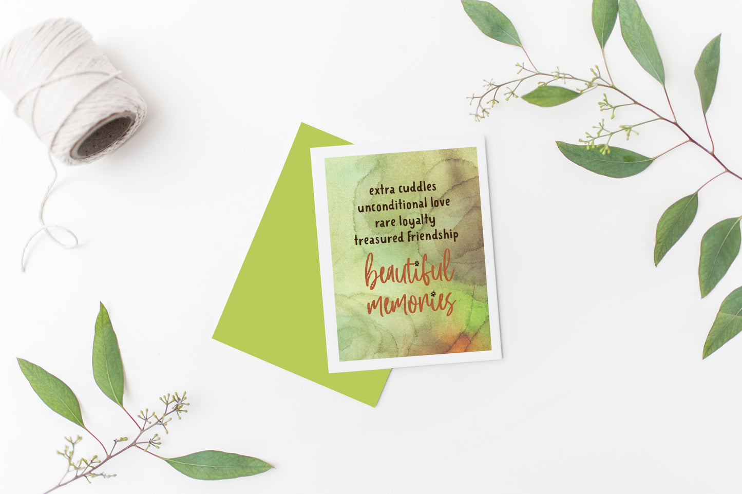 Greeting card laying on a white background near green leaves and a spool of white string.