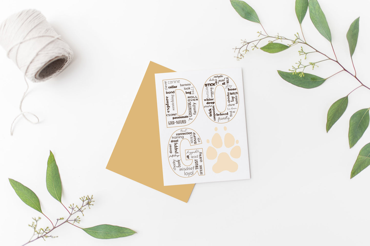 Greeting card laying on a white background near green leaves and a spool of white string.