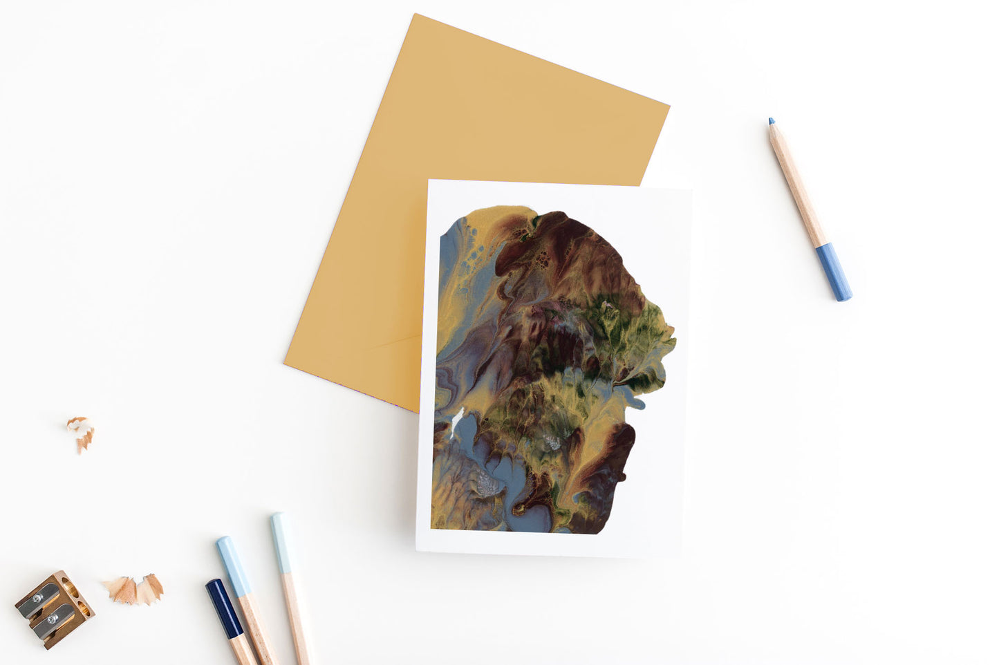 Greeting card, seen from above, with a colored, square flap envelope, pencils, pencil sharpener and shavings on a white background.
