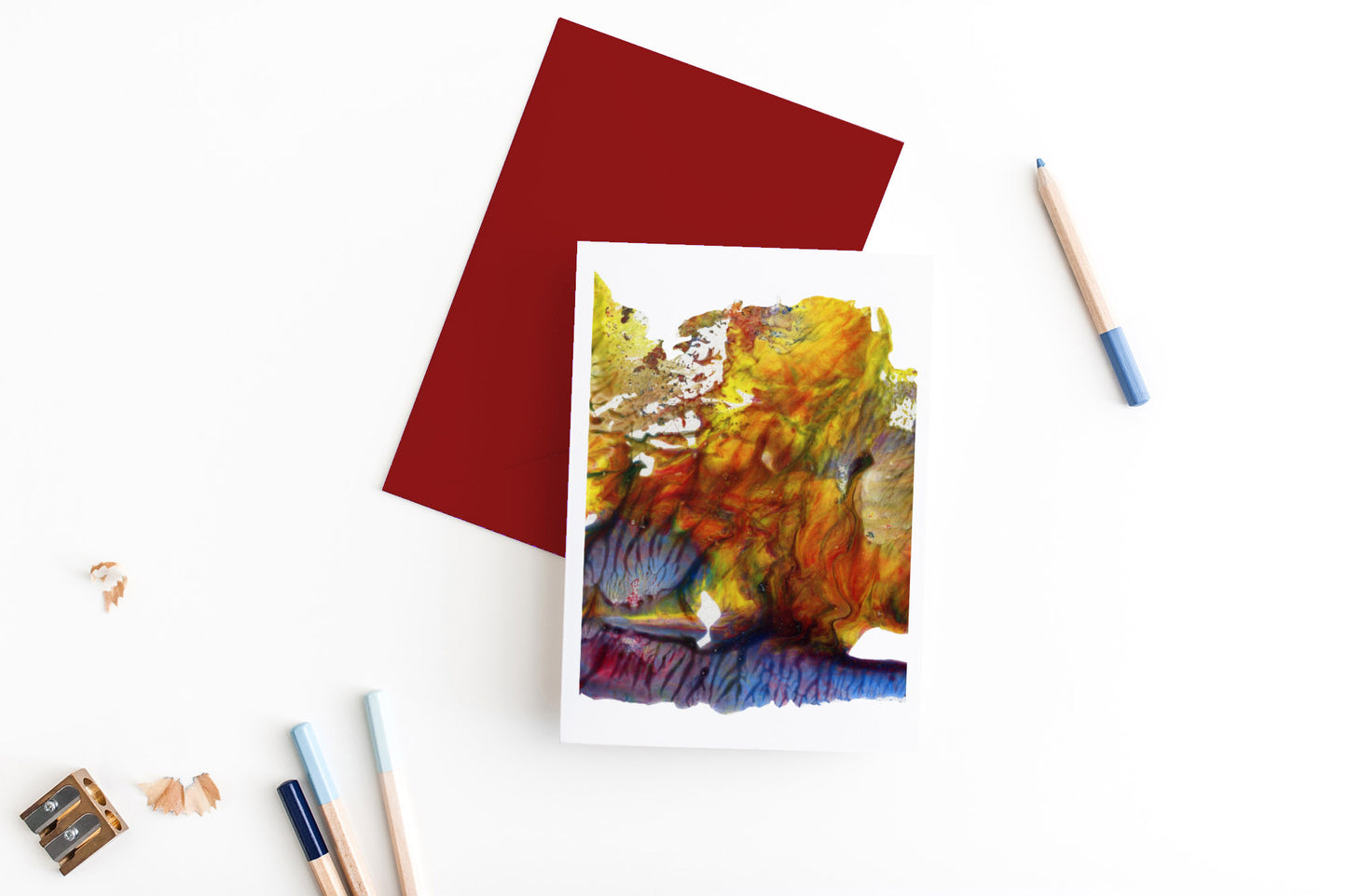 Greeting card, seen from above, with a colored, square flap envelope, pencils, pencil sharpener and shavings on a white background.