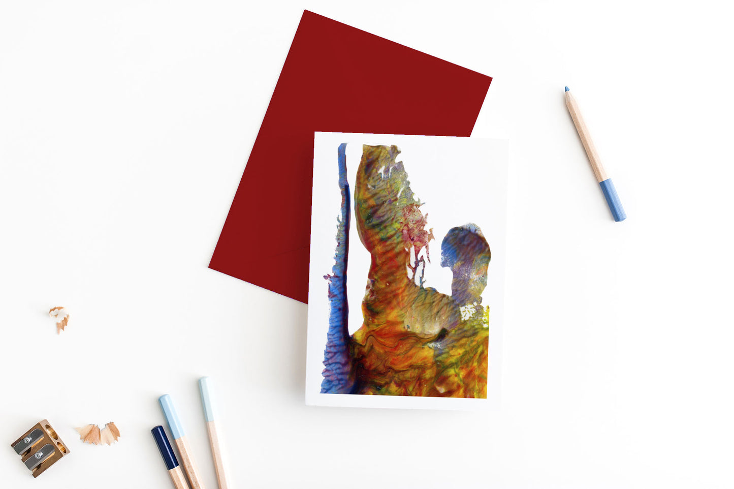 Greeting card, seen from above, with a colored, square flap envelope, pencils, pencil sharpener and shavings on a white background.