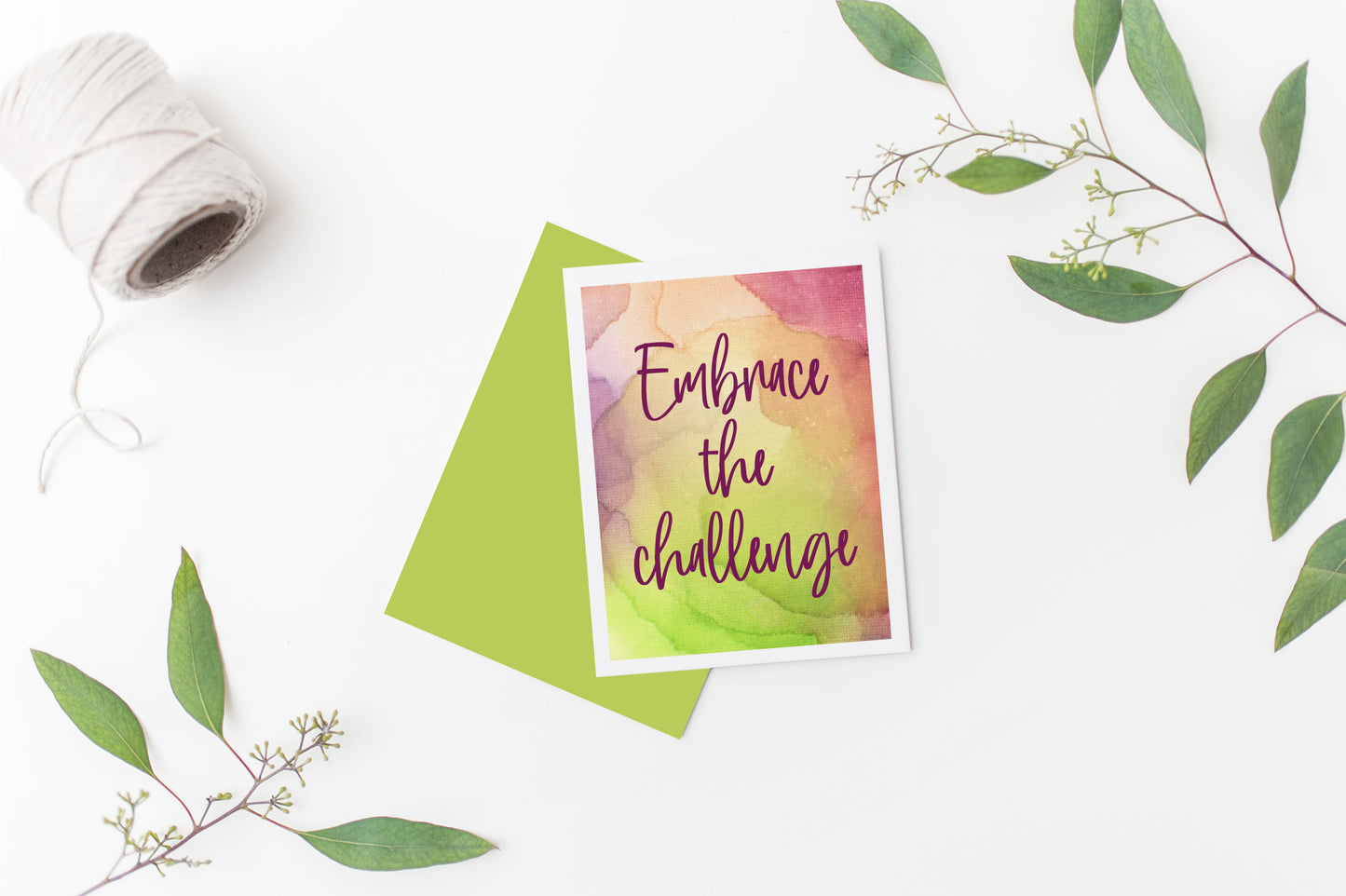 Greeting card laying on a white background near green leaves and a spool of white string.