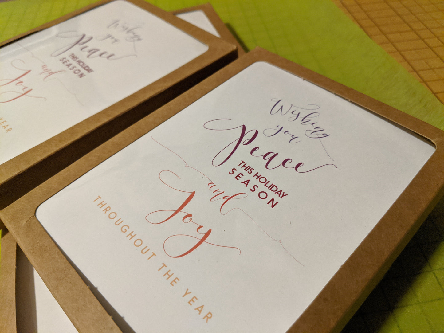 Angled view of greeting cards in kraft boxes laying on bright green tissue.