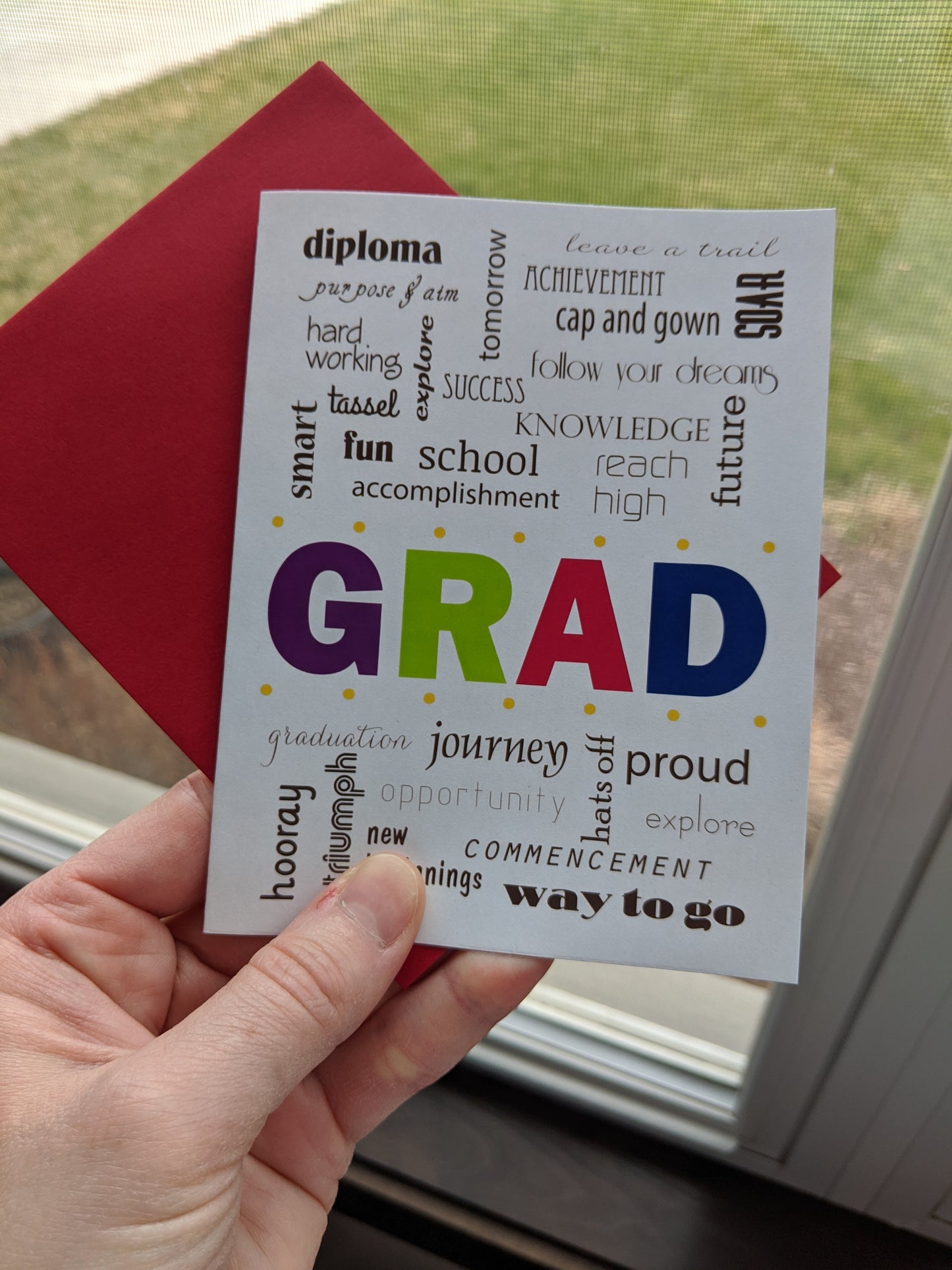 Hand holding a greeting card and colorful envelope near a window.