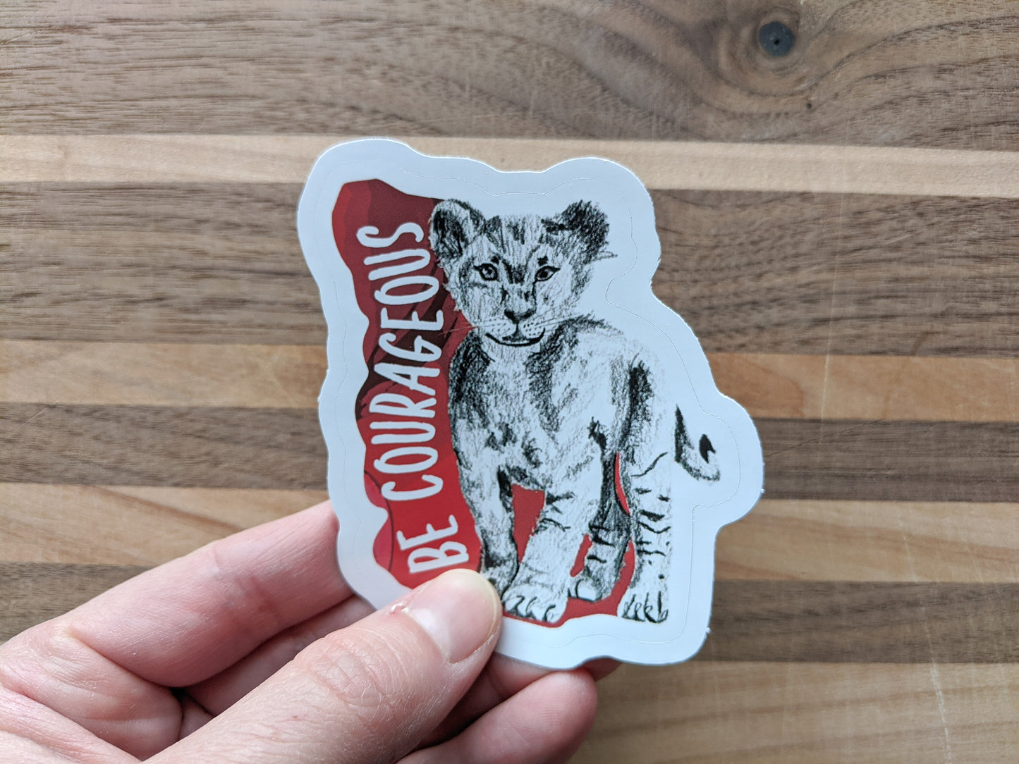 Hand holding a sticker with a wooden surface in the background.