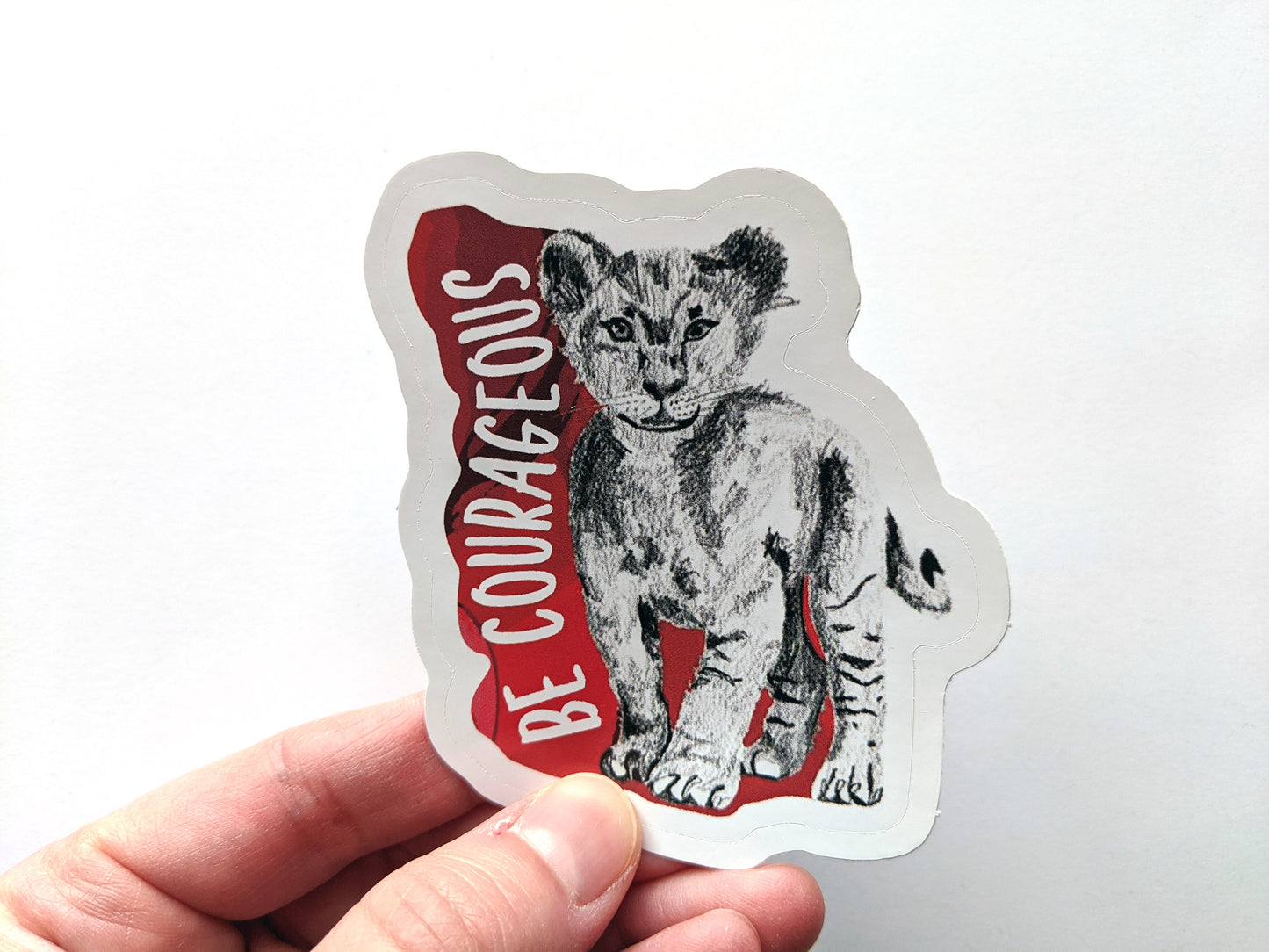 Hand holding a sticker with a white surface in the background.