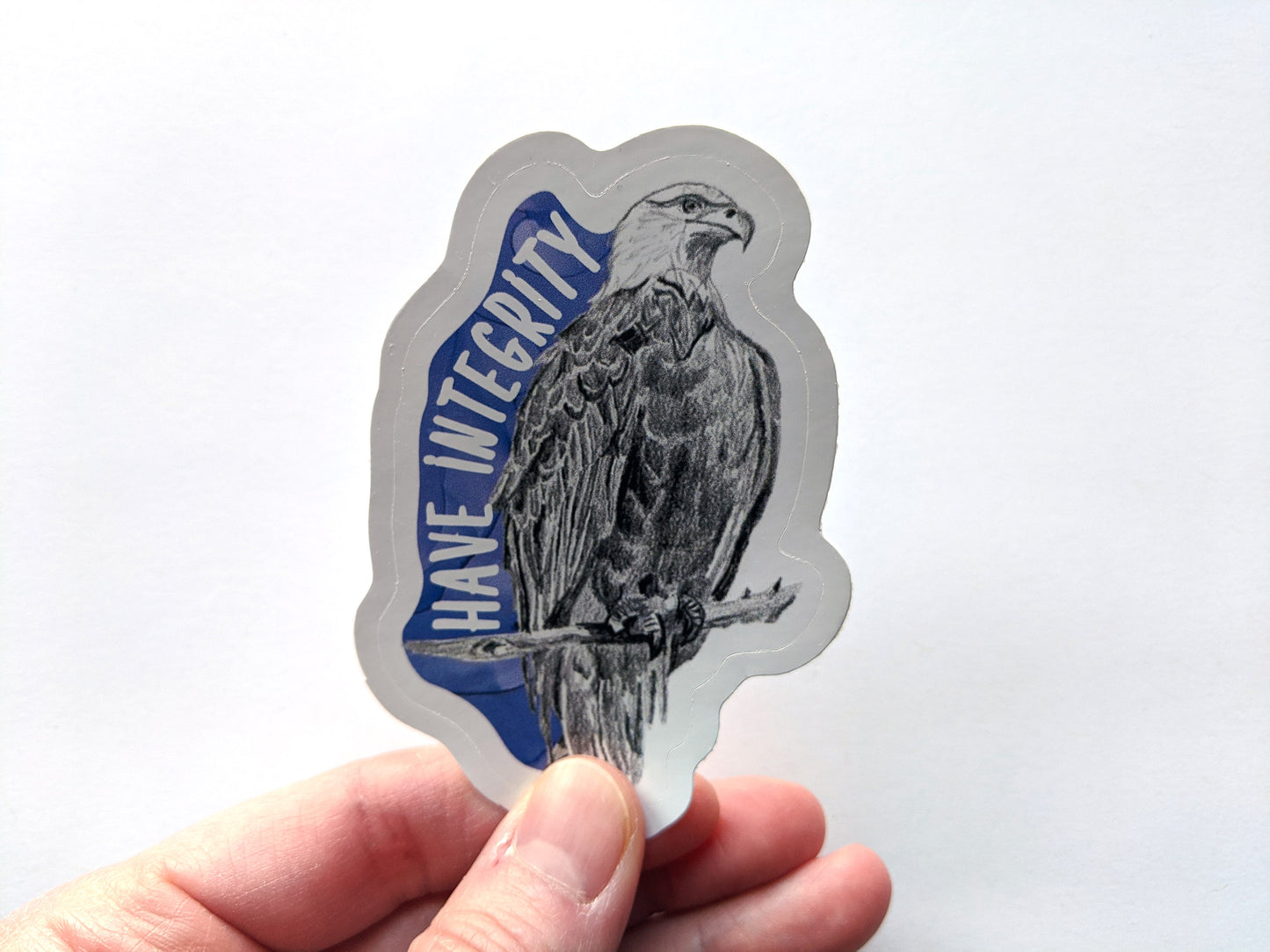 Hand holding a sticker with a white surface in the background.