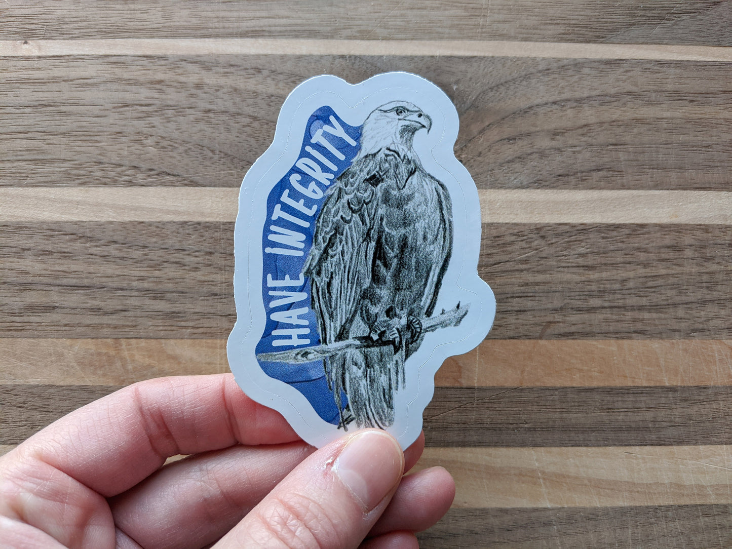 Hand holding a sticker with a wooden surface in the background.