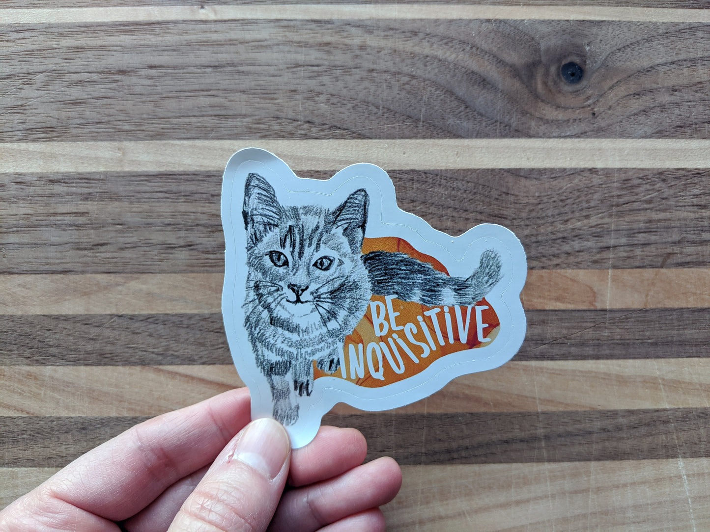 Hand holding a sticker with a wooden surface in the background.