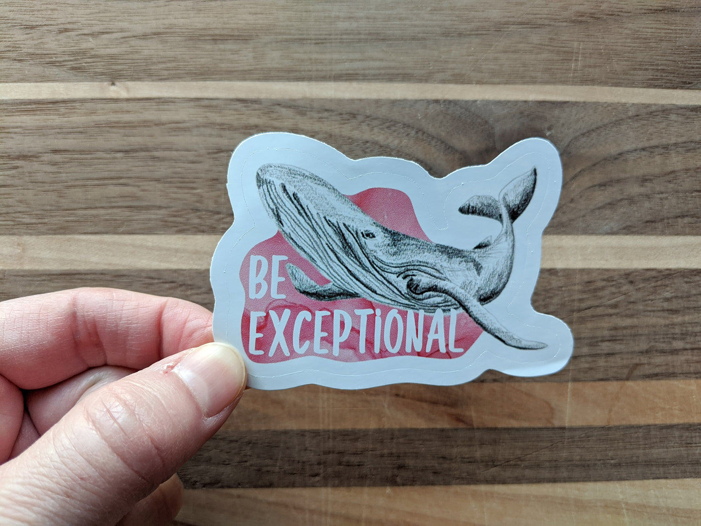 Hand holding a sticker with a wooden surface in the background.