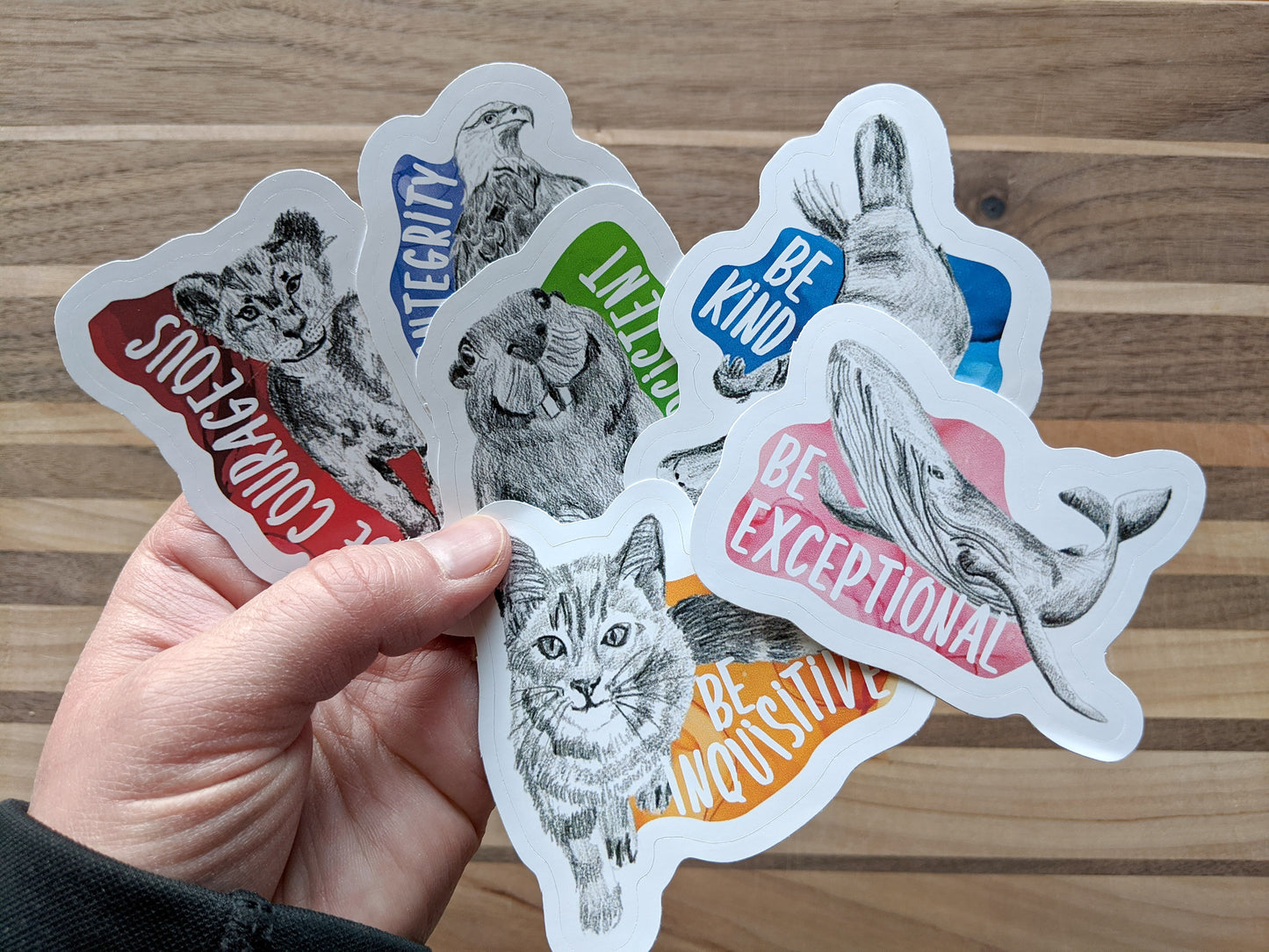 Hand holding six overlapping stickers above a wooden background.