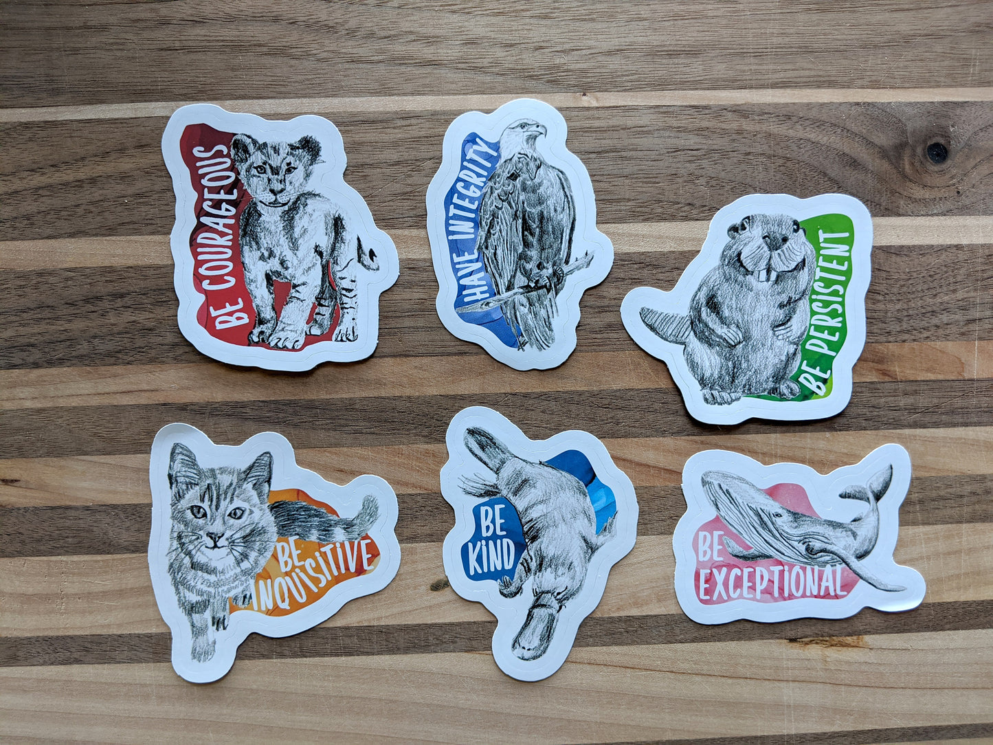 Six stickers laying on a wooden surface.