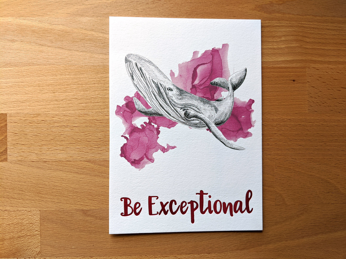 Art print accented in foil laying on a wooden tabletop.