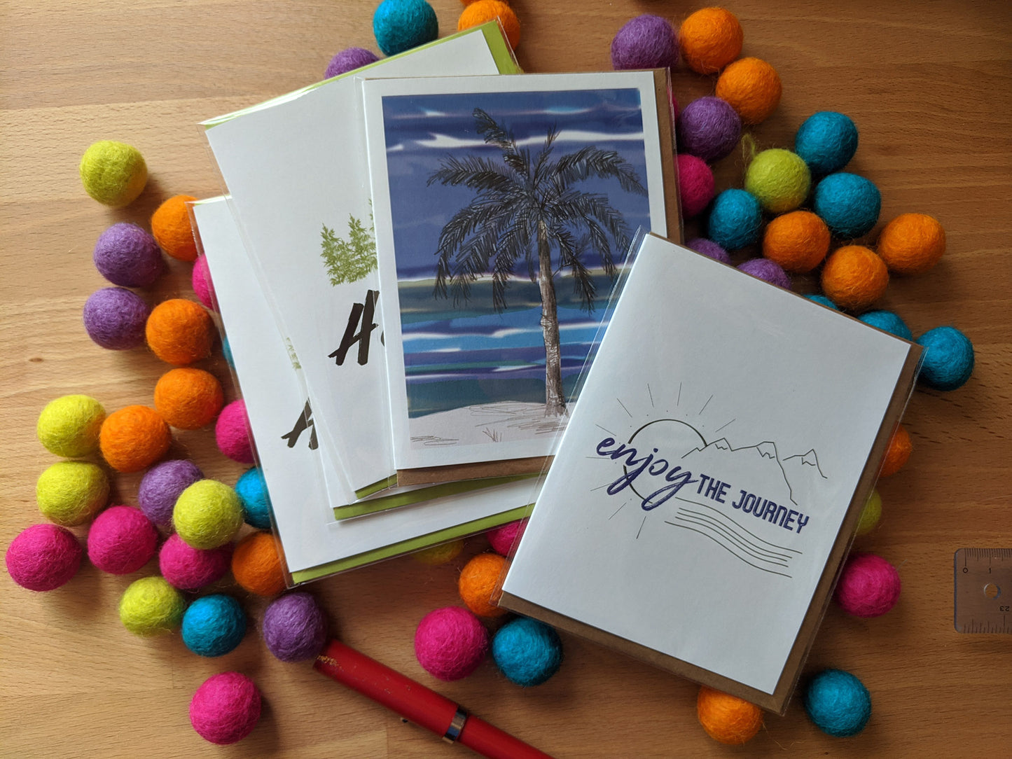 Five greeting cards overlapping on a pile of colorful felt balls and a pen.