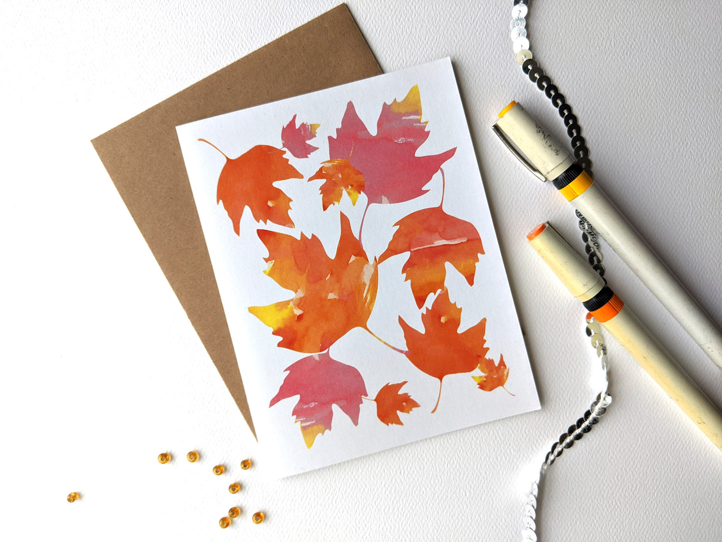 Greeting card and envelope on a white background with tiny beads, sequins and two pens.