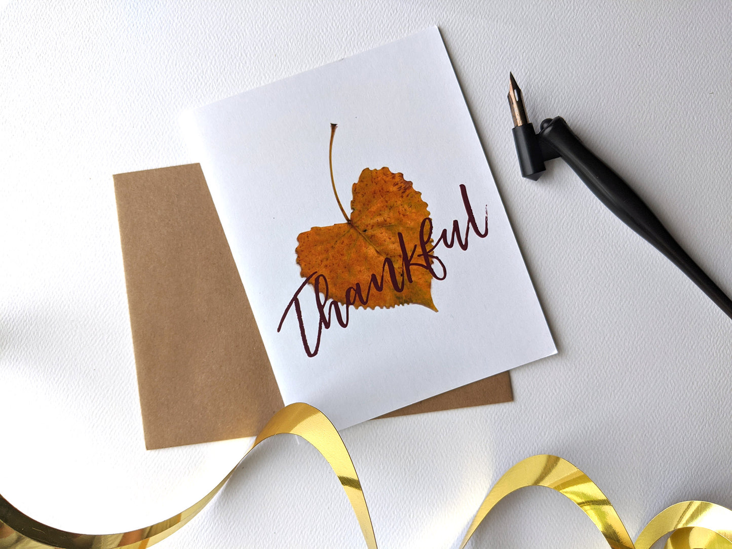 Greeting card and kraft envelope, seen from above, on a white background with gold spiral party decor and a black calligraphy pen.
