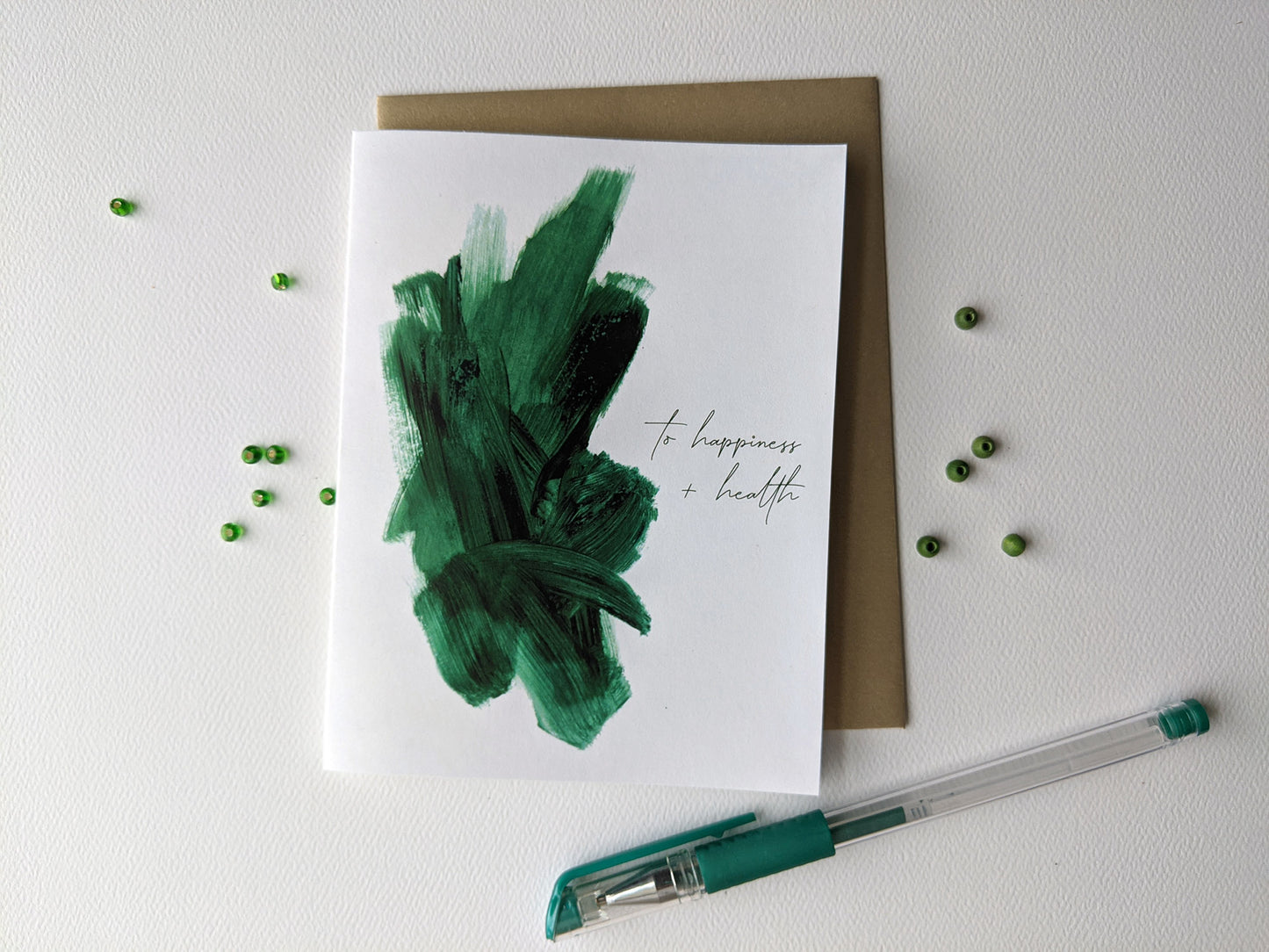 Greeting card with colorful envelope on a white background with tiny beads and a pen.