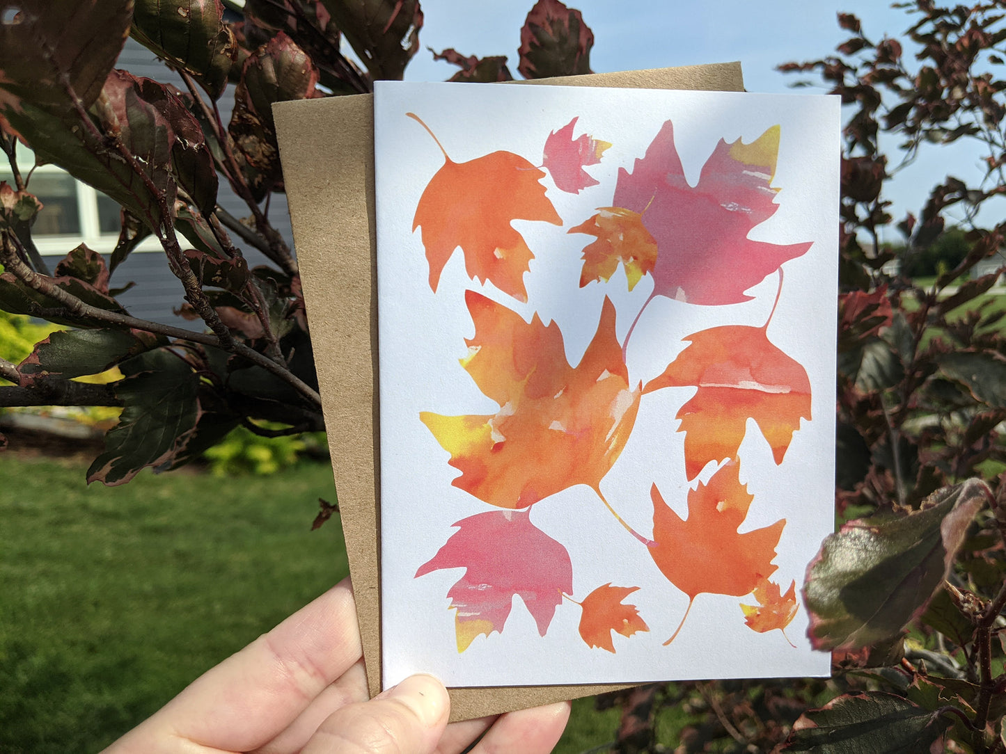 Hand holding greeting card with shrub leaves in the background.