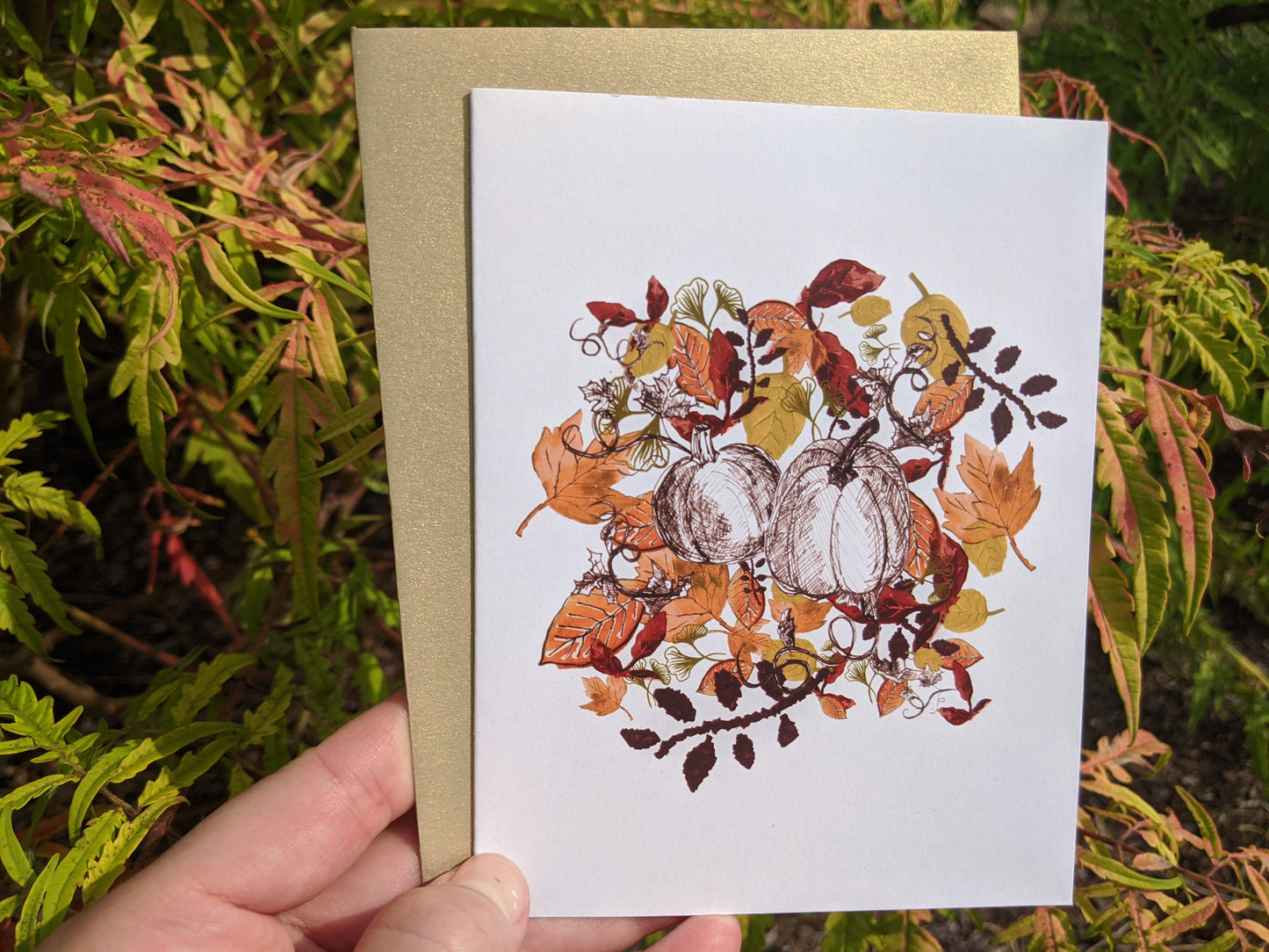 Hand holding a greeting card with shrubs in the background.