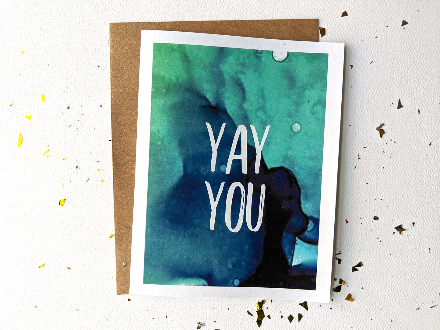 Greeting card laying flat with an envelope on a white background with gold confetti surrounding it.