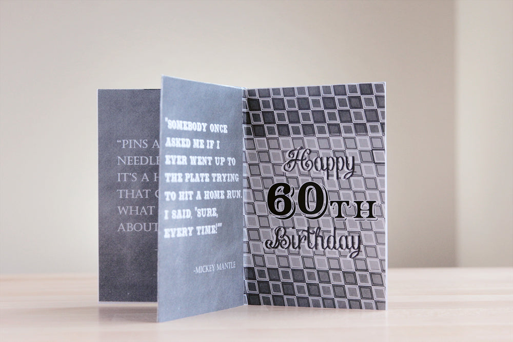 Centerpiece sitting on a wooden table with a neutral wall in the background. The chalkboard texture of the panels includes favorite quotes and another geometric graphic pattern includes the words Happy 60th Birthday.