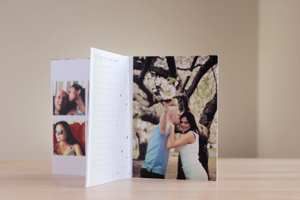 Centerpiece standing on a wooden table top showing an engagement photo of a coupl standing under tree branches, lyrics to a favorite song, and candid snapshots of them together.