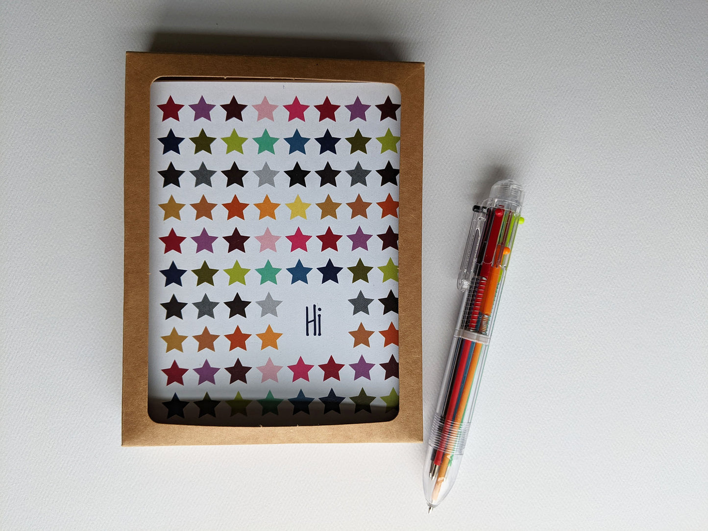 Greeting card in a recyled kraft box next to a multicolored pen on a white background.