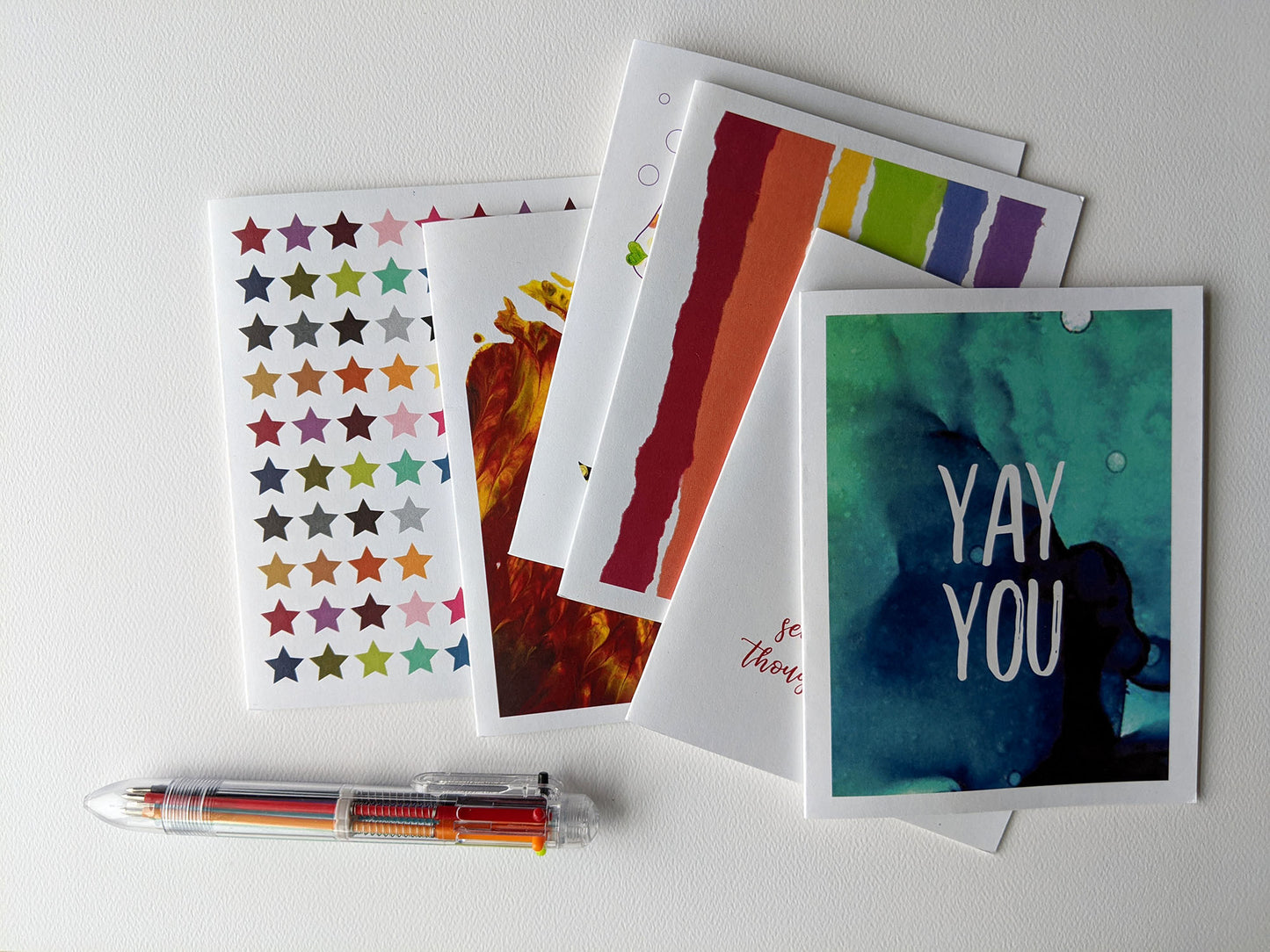 Overlapping greeting cards on a white background shown with a multicolored pen.
