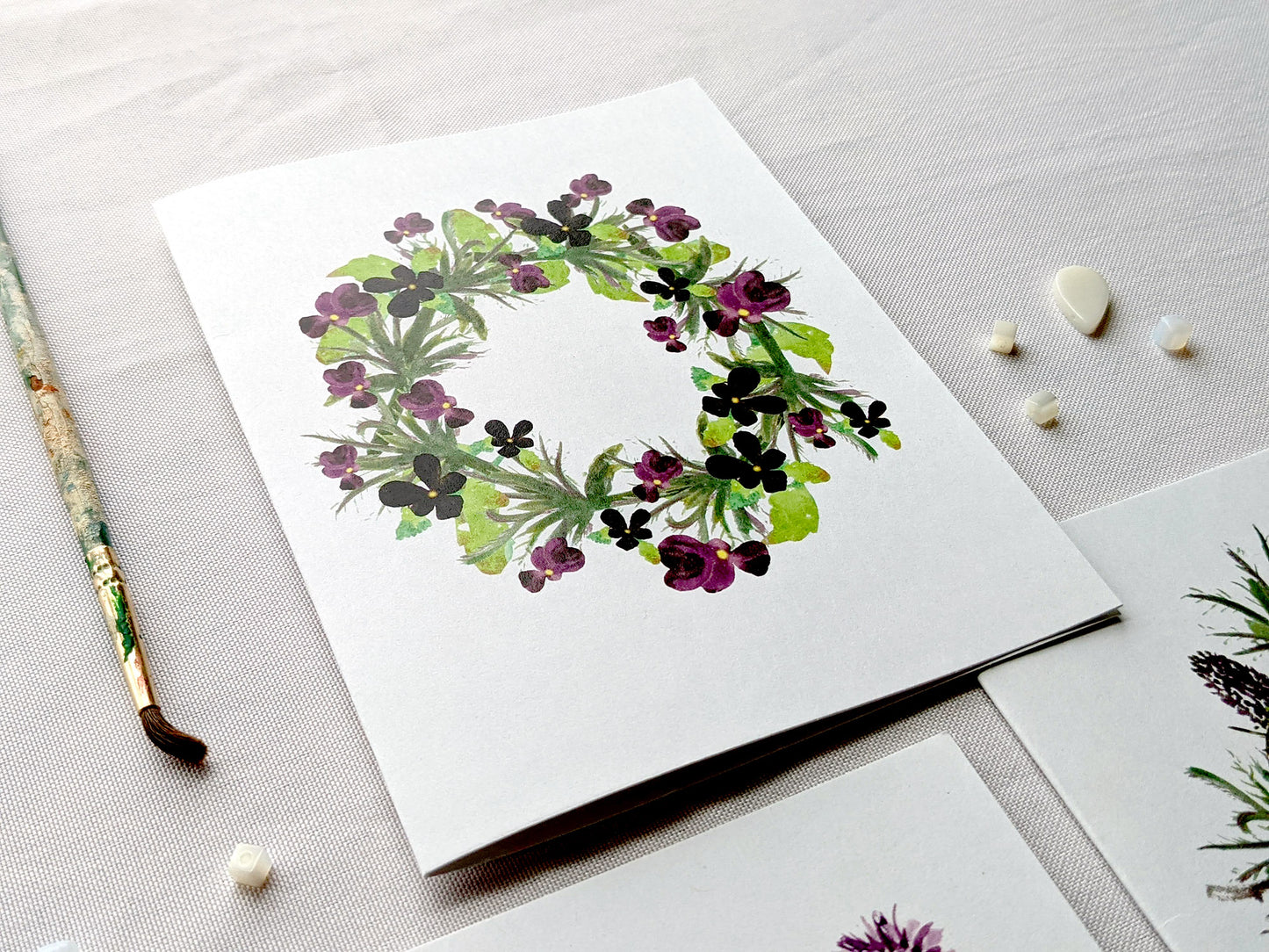 Angled view of greeting cards on a white surface with beads and paint brush.