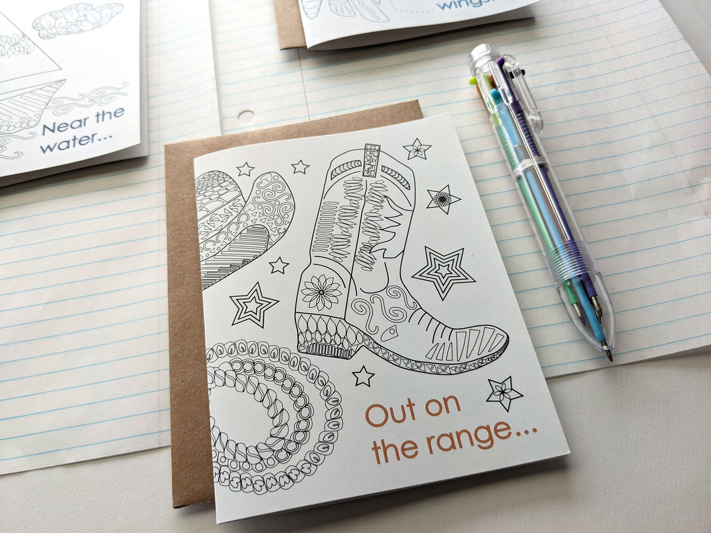 Angled view of greeting cards laying on lined notebook paper and multi-colored pen.