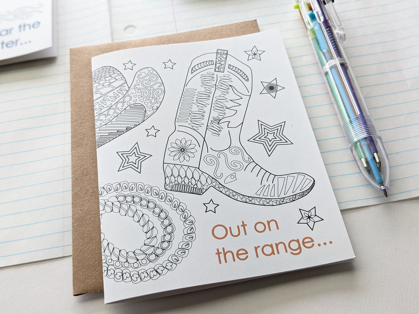 Angled view of greeting cards laying on lined notebook paper and multi-colored pen.