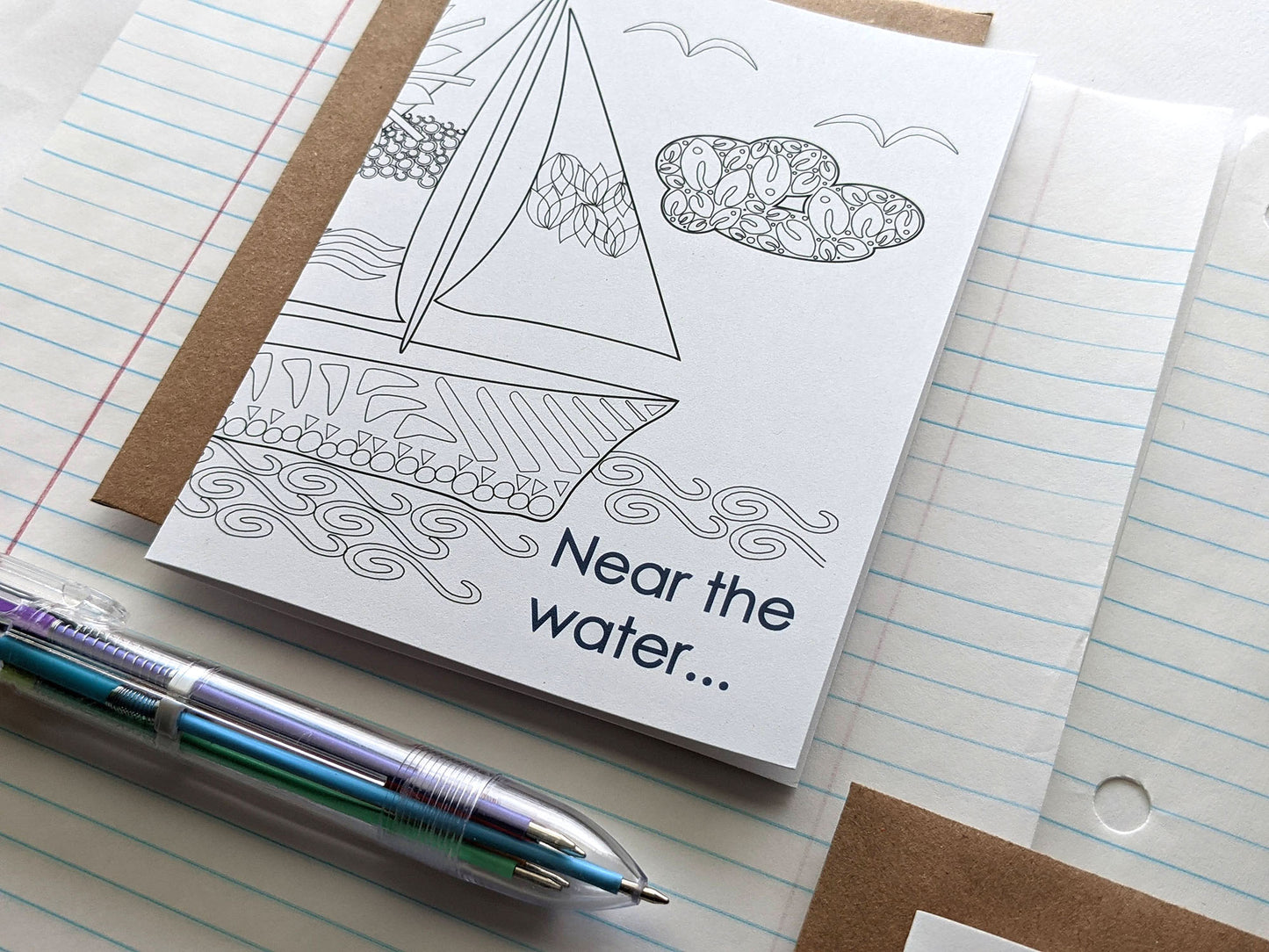 Angled view of greeting cards laying on lined notebook paper and multi-colored pen.
