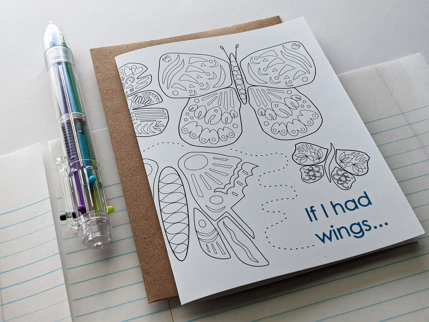 Angled view of a greeting card laying on lined notebook paper with a multi-colored pen.