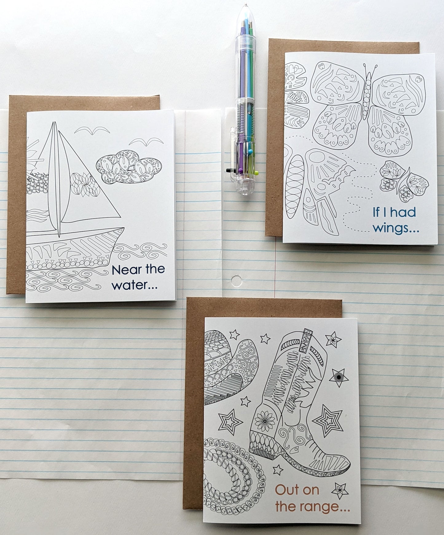 Three greeting cards laying on lined notebook paper with a multi-colored pen.