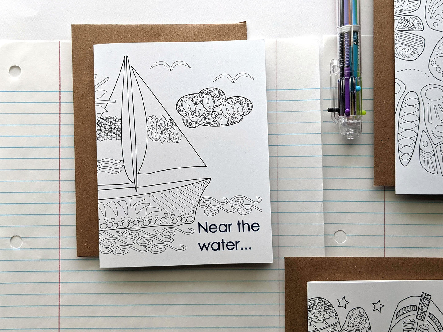 Three greeting cards laying on lined notebook paper with a multi-colored pen.