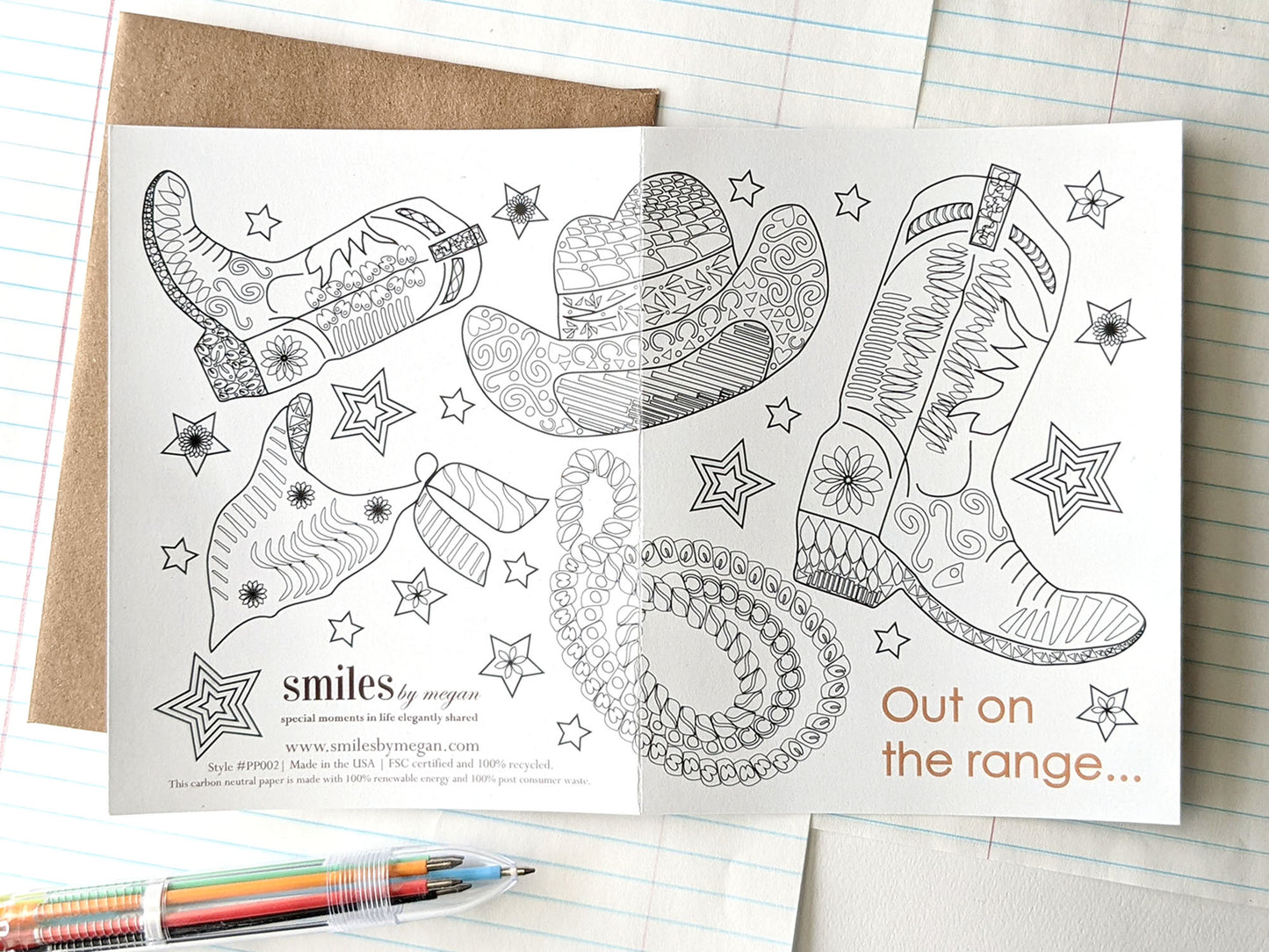 Open greeting card showing the image spanning both the back and the front with a kraft envelope, lined notebook paper and a multi-colored pen.