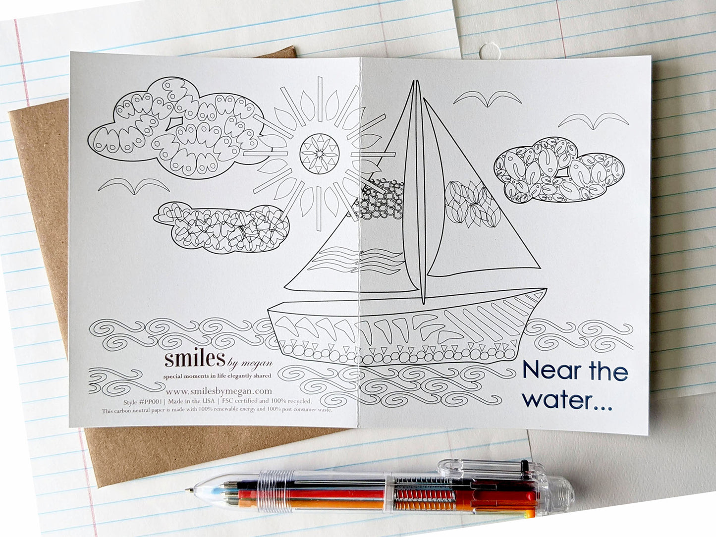 Open greeting card showing the image spanning both the back and the front with a kraft envelope, lined notebook paper and a multi-colored pen.