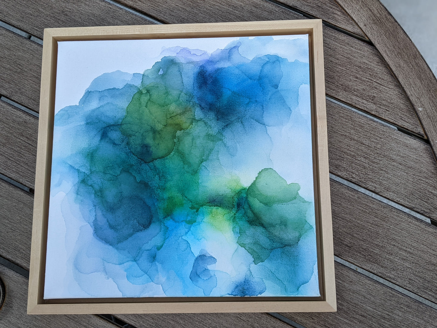 Photo from above of the canvas in a light maple float frame laying on a slat patio table.