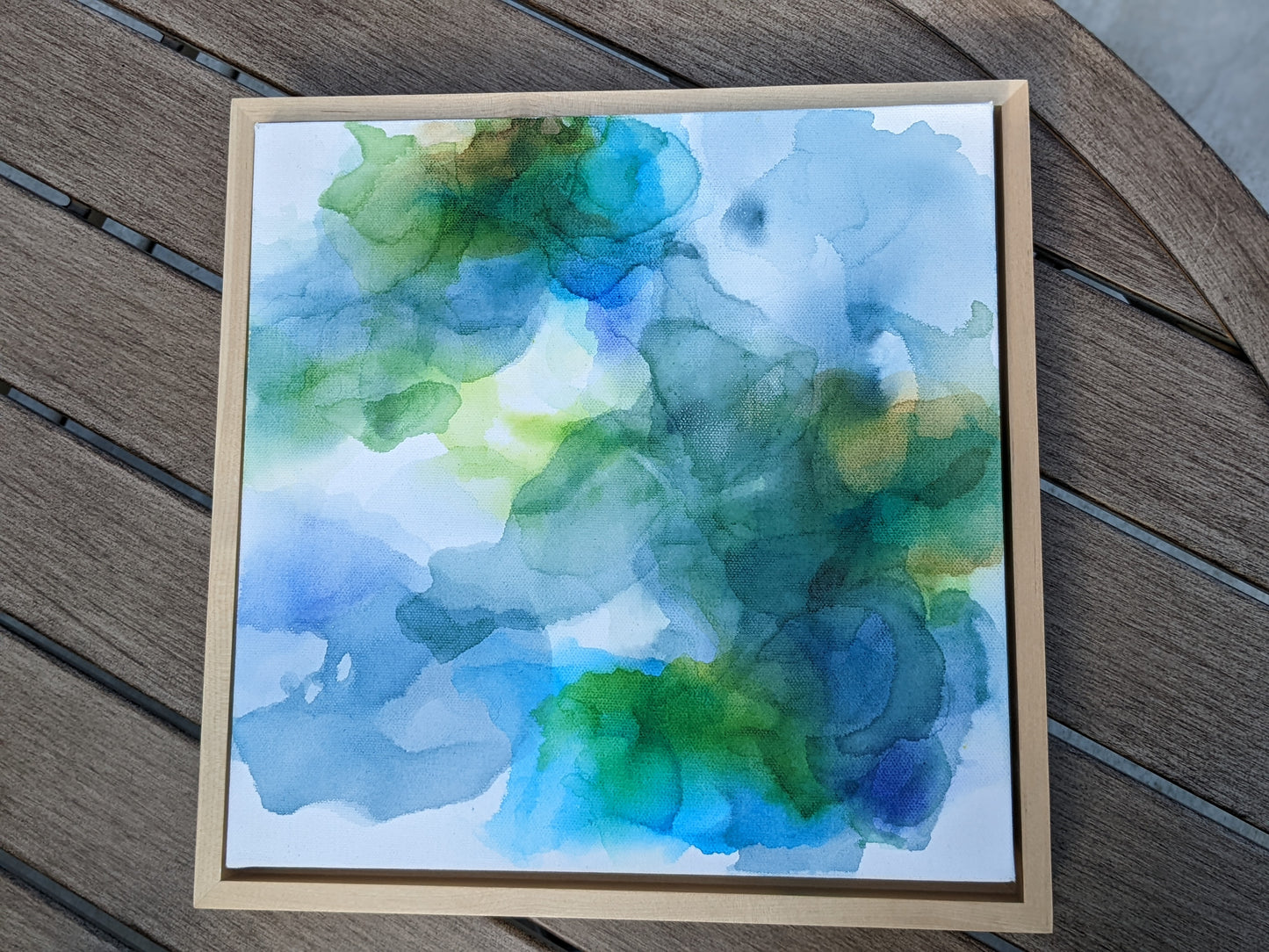Photo from above of the canvas in a light maple float frame laying on a slat patio table.