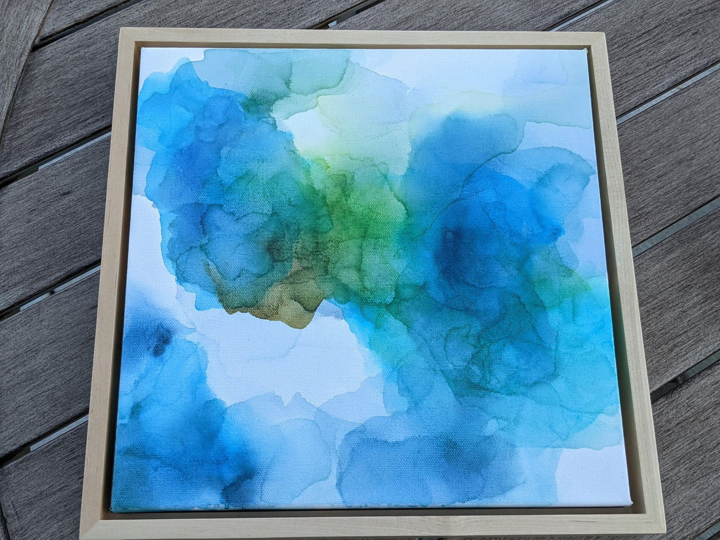 Photo from above of the canvas in a light maple float frame laying on a slat patio table.
