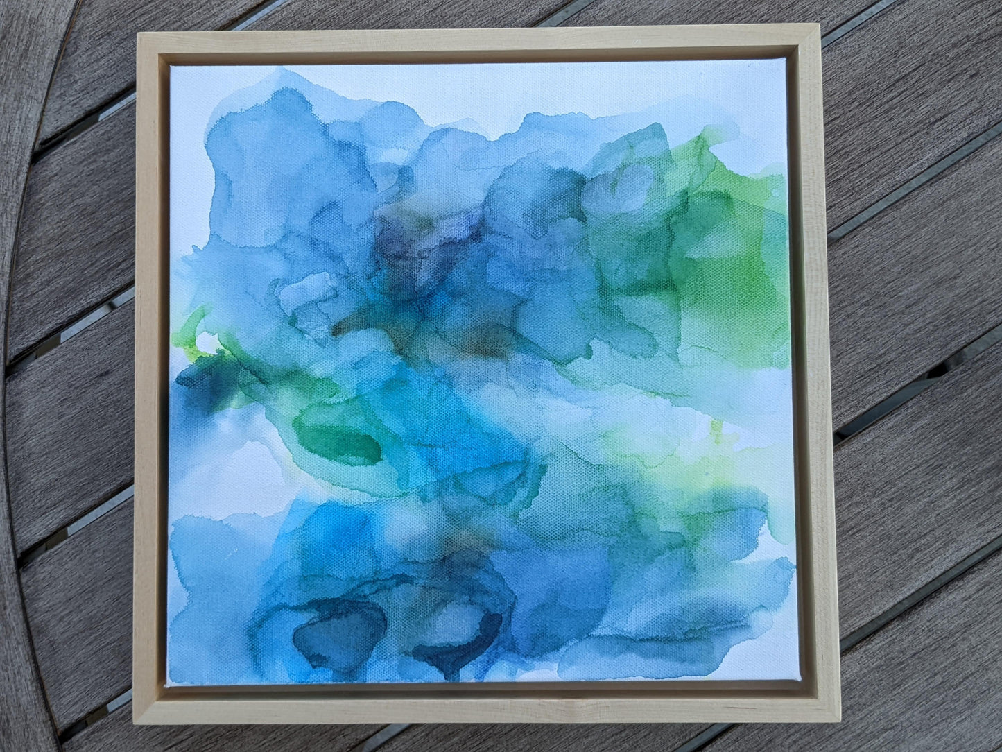 Photo from above of the canvas in a light maple float frame laying on a slat patio table.