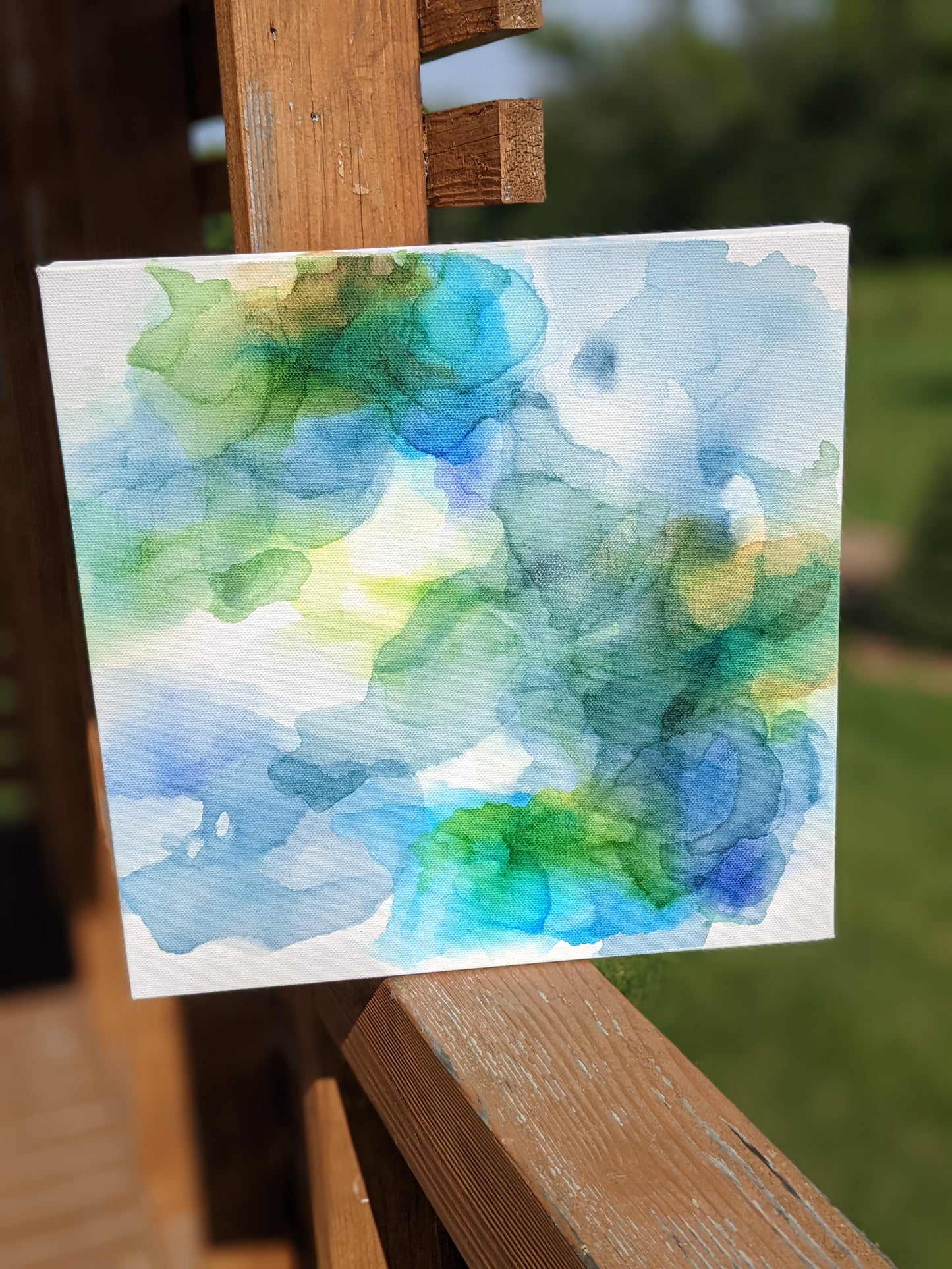 Canvas shown outdoors sitting on a wooden railing with greenery in the background.