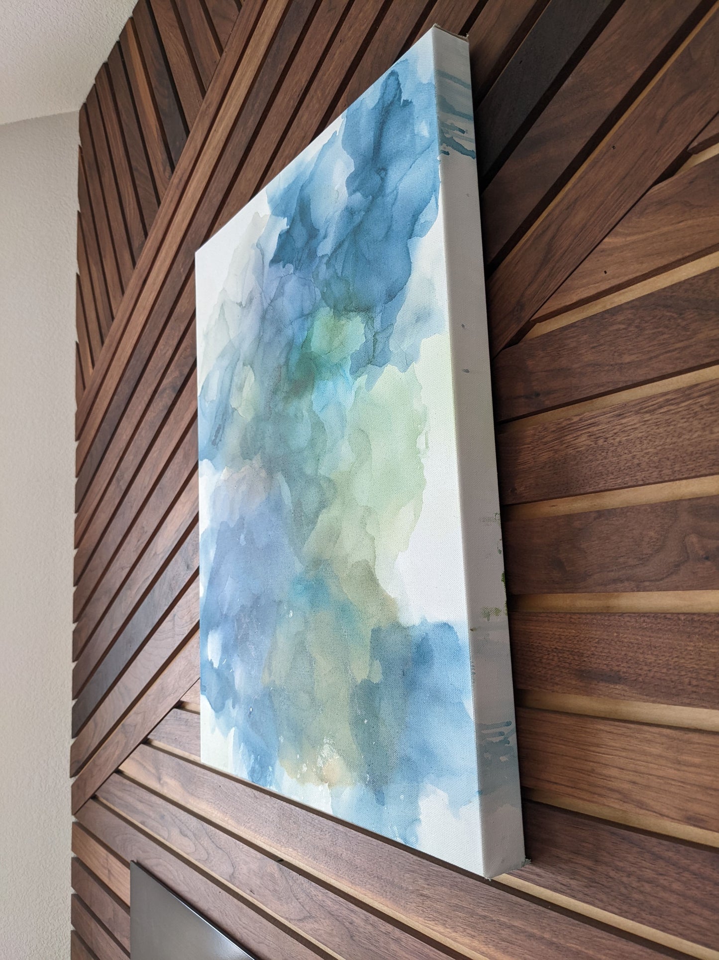 Angled side view of canvas hanging on a wood slat wall.
