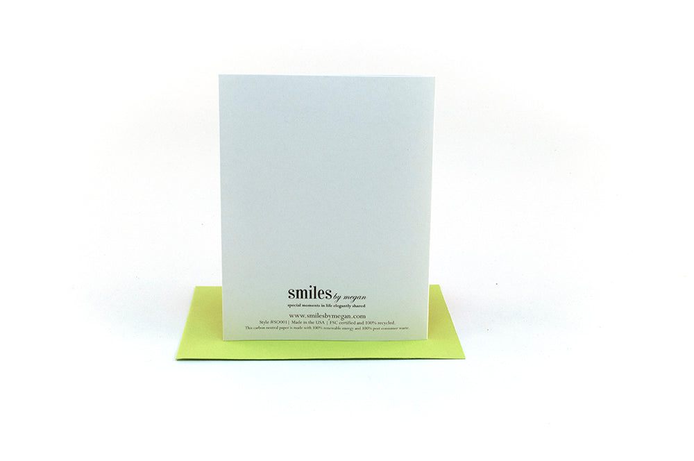 Back side of greeting card standing upright on top of a colorful envelope against a white background.