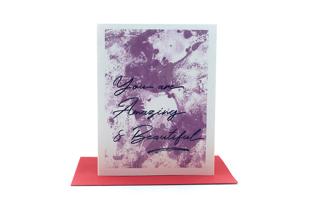 Greeting card standing upright on top of a colorful envelope against a white background.