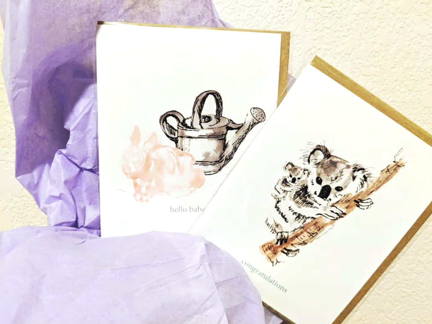 Two greeting cards with lilac tissue paper against a white wall.