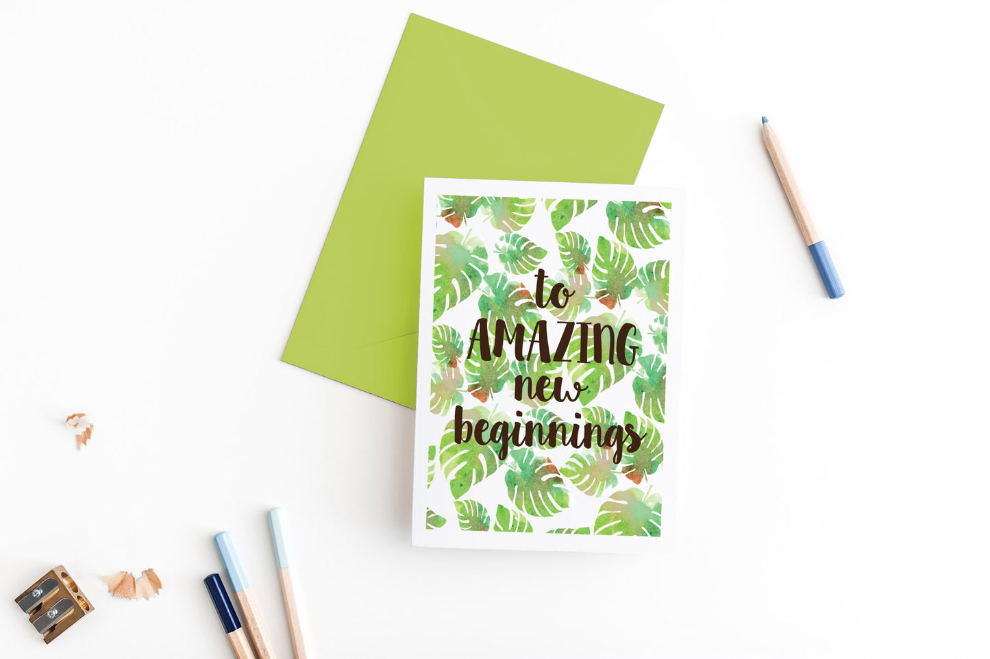 Greeting card, seen from above, with a colored, square flap envelope, pencils, pencil sharpener and shavings on a white background.
