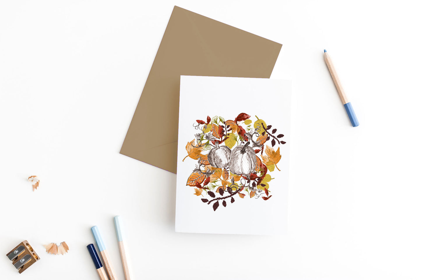 Greeting card, seen from above, with a colored, square flap envelope, pencils, pencil sharpener and shavings on a white background.